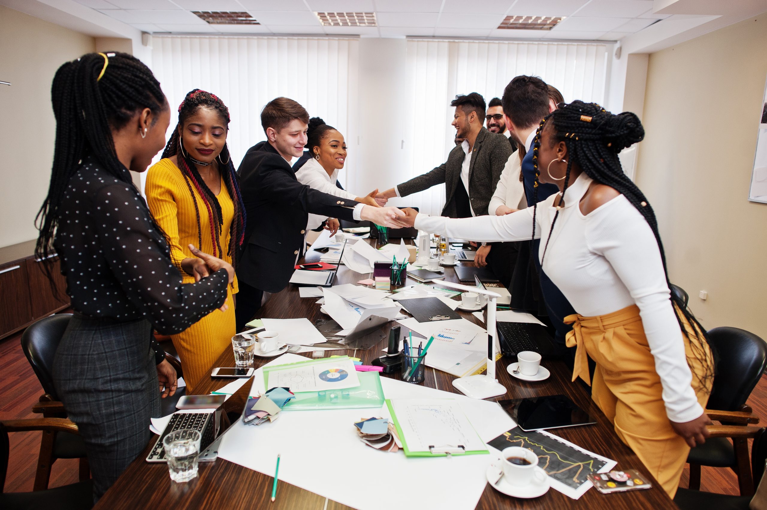 Good deal. Multiracial business team addressing meeting around boardroom table and shaking hands each other.